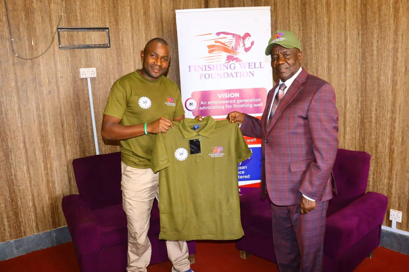 A Finishing Well Foundation team member and an elder holding up the foundation's olive-green polo shirt